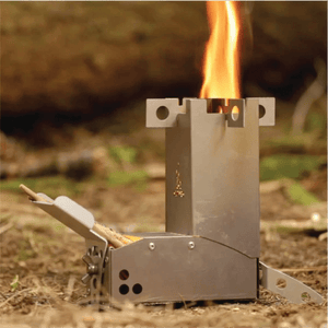 A Hot Ash rocket stove with a tall, intense flame burning from the top, fueled by small sticks in the feeder, set up outdoors on the forest floor.