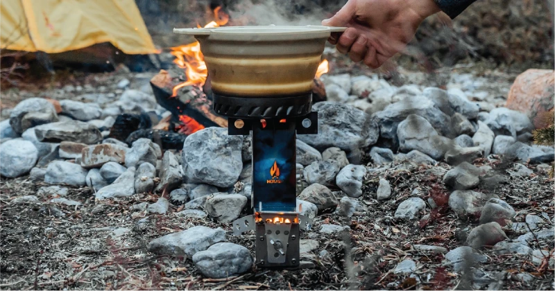 Hot Ash rocket stove cooking over a campfire with tent in background